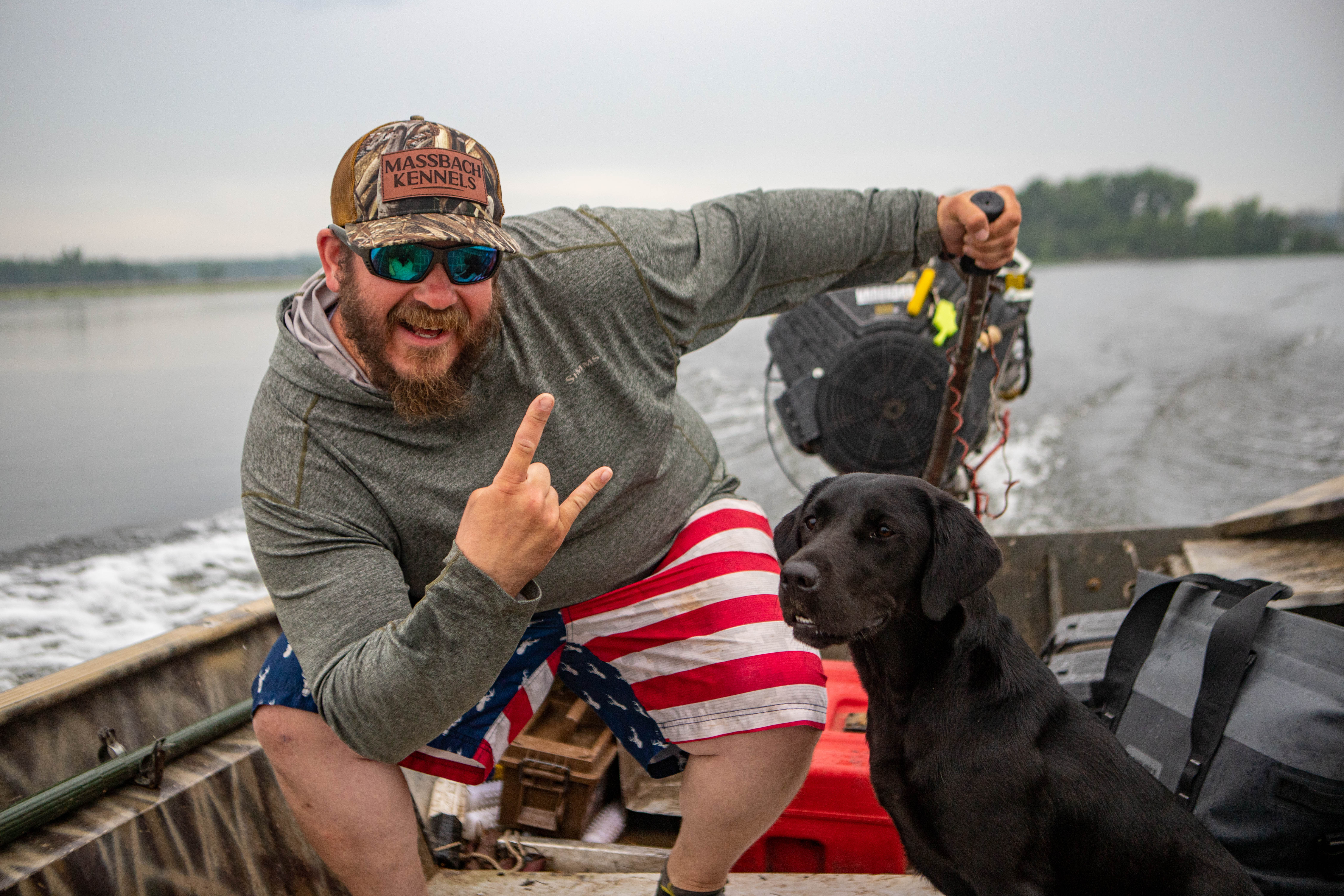 Trainer with black lab on boat with hunting gear